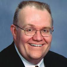 A man with glasses and a beard wearing a suit.