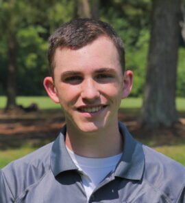 A young man standing in front of some trees.