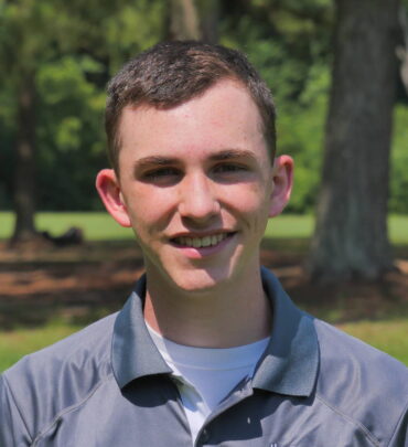 A young man standing in front of some trees.