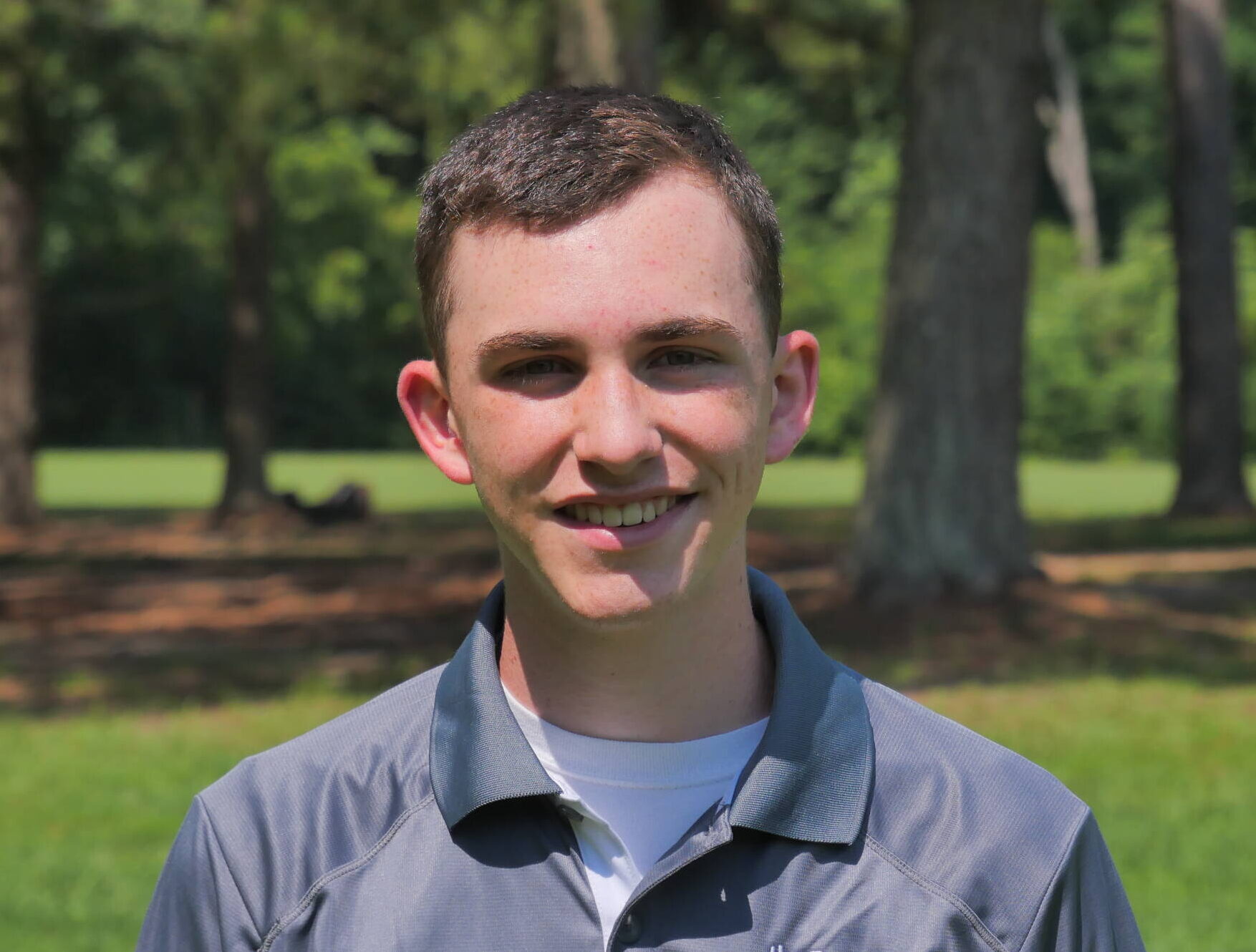A young man standing in front of some trees.