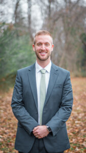 A smiling man in a suit and tie outdoors.