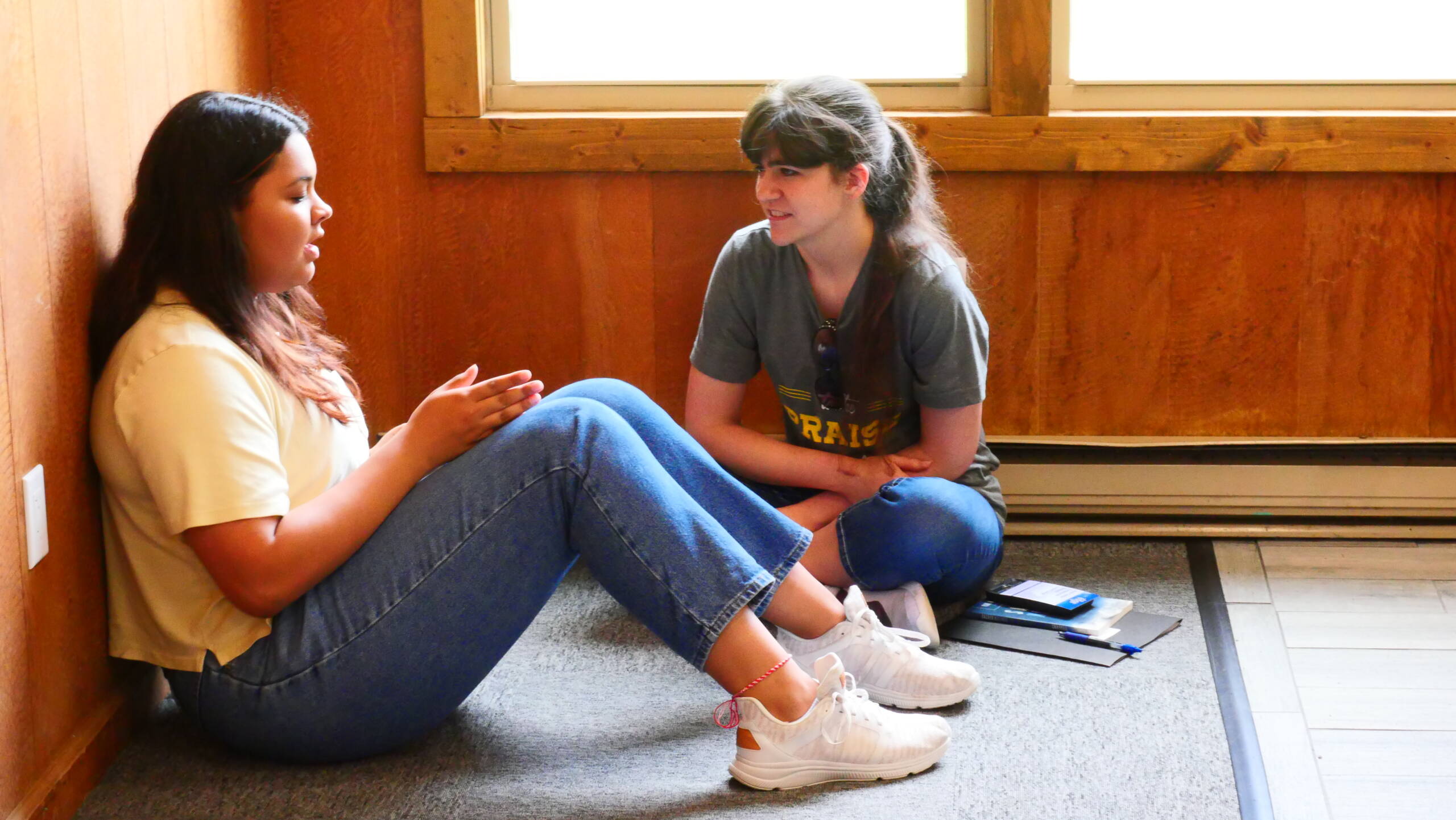 Two women sitting on the ground talking to each other.