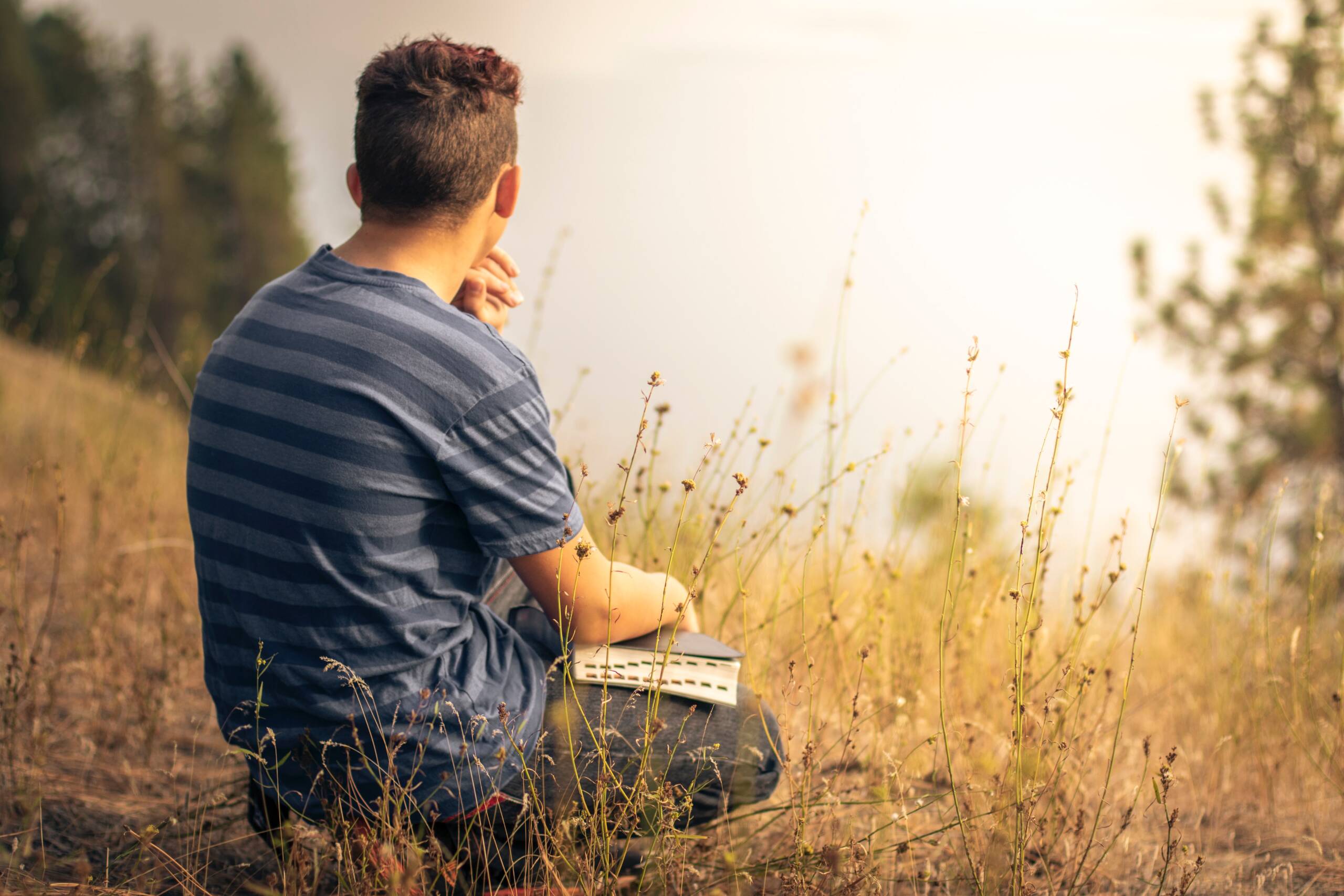 A man sitting in the grass with his hand on his chin.