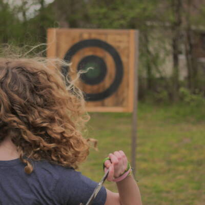 A woman is holding her arm out to hit an arrow.