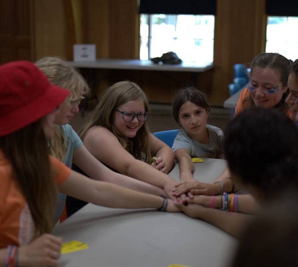 A group of people sitting around a table holding hands.