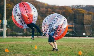 Two people playing zorbing outdoors on grass.
