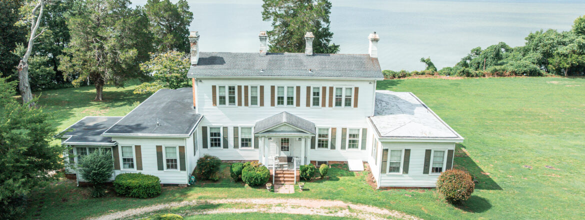 Large white colonial-style house with a waterfront view and manicured lawn.