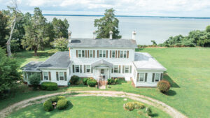 Large white colonial-style house with a waterfront view and manicured lawn.