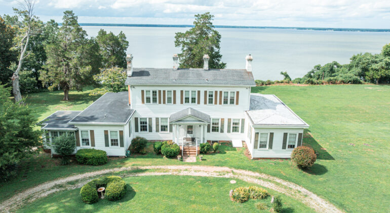 Large white colonial-style house with a waterfront view and manicured lawn.