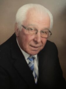 Elderly man in glasses and suit with a striped tie.