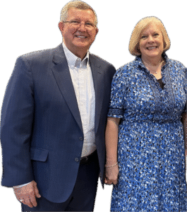 A smiling man in a suit next to a woman in a blue floral dress.